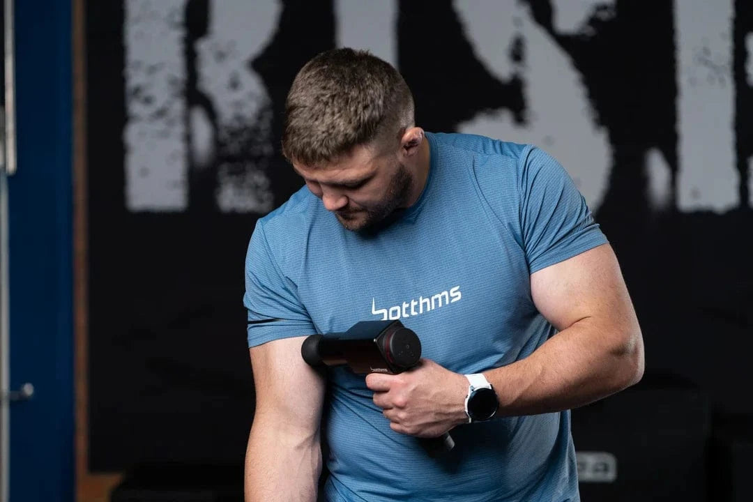 man applying botthms massage gun on his right arm muscle
