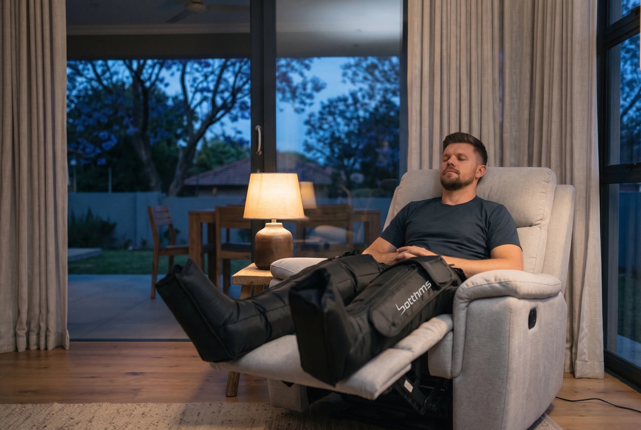 Man relaxing in a recliner wearing botthms recovery boots in a Johannesburg lounge at dusk