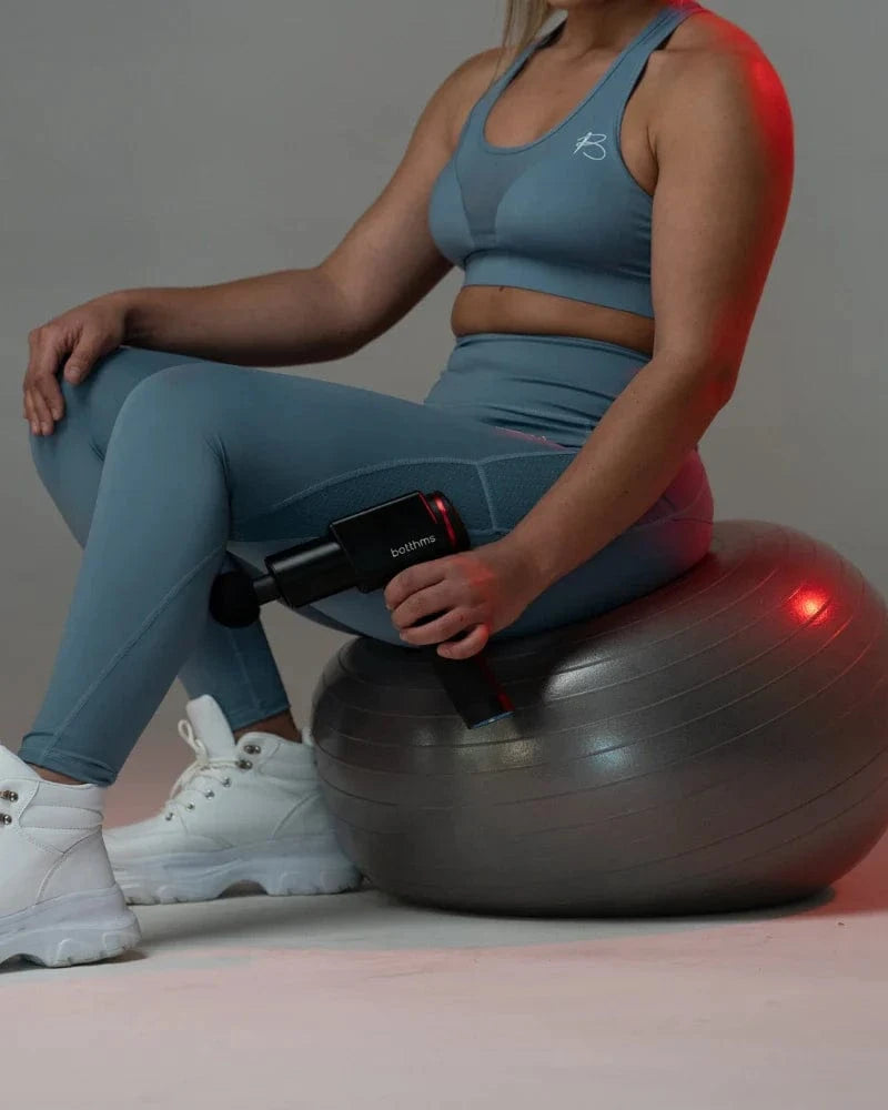 young blonde trying botthms massage gun on her left leg lower part muscle