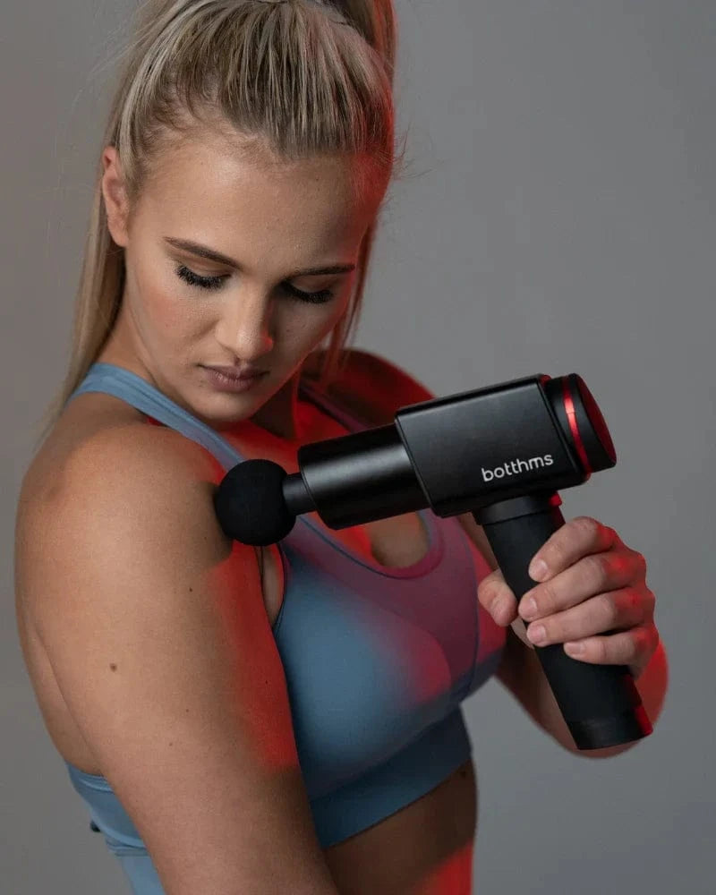 Young blonde trying botthms massage gun on her left shoulder